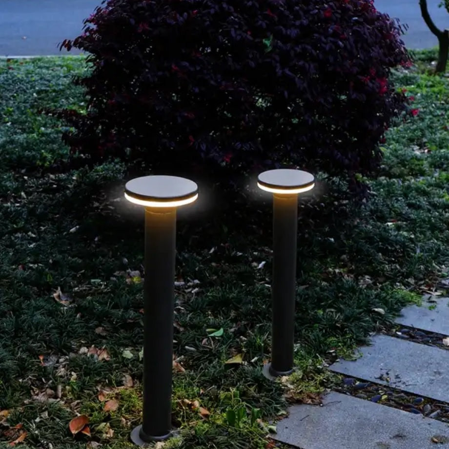 Twee moderne zwarte tuinpalen met ronde LED-verlichting, geplaatst langs een tuinpad in een avondsetting – frontaal aanzicht.