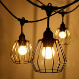 Close-up van industriële stringlight buitenlampen met metalen kooikap en warme LED-verlichting, hangend in een sfeervolle avondsetting.