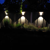 Moderne buitenwandlampen met up- en downlight verlichting gemonteerd op een houten schutting, verlichtend effect in de vorm van een X zichtbaar in nachtelijke tuinsetting, vooraanzicht.