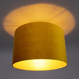 Gele velvet plafondlamp met cilinder vorm, gezien van schuin onderaanzicht, met warm licht dat een zachte gloed op het plafond werpt.
