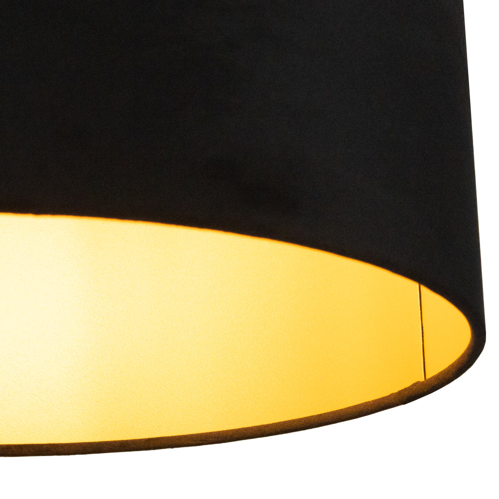 Zijaanzicht van een zwarte plafondlampenkap met goudkleurige binnenzijde die warm licht uitstraalt.