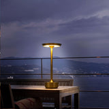 Gouden tafellamp met modern design op houten buitentafel, verlicht in schemering met uitzicht op berglandschap en zee – zijaanzicht.