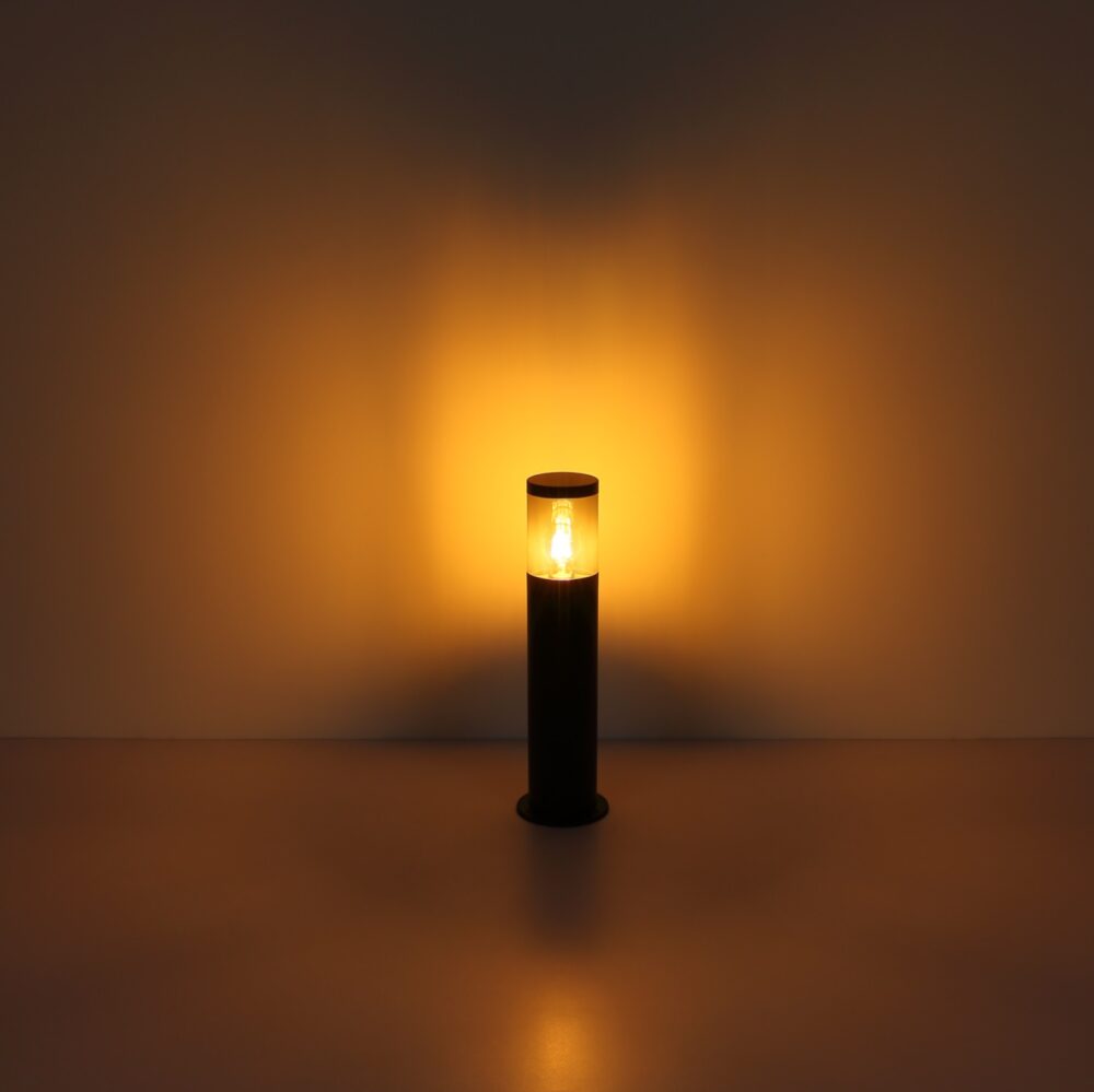 Zwarte moderne buitenlamp sokkelverlichting met warm wit licht aan, frontaal aanzicht tegen een neutrale achtergrond.