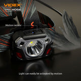 Close-up vooraanzicht van de VIDEX HO56 hoofdlamp met bewegingssensor, geactiveerd door een handbeweging, op een zwarte achtergrond met duidelijke weergave van LED-lamp, bedieningsknoppen en verstelbare hoofdband.