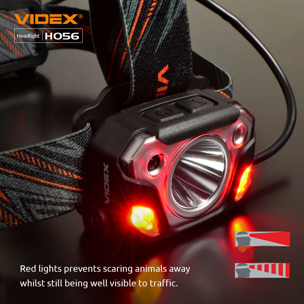 Close-up vooraanzicht van de VIDEX HO56 hoofdlamp met rood waarschuwingslicht aan beide zijden, bevestigt aan een verstelbare hoofdband met zwart-oranje patroon, ontworpen voor zichtbaarheid in het donker zonder dieren te verjagen.