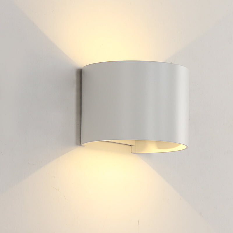 Moderne witte wandlamp met omhoog en omlaag schijnend licht, cilindrisch ontwerp, zijaanzicht tegen een witte muur.