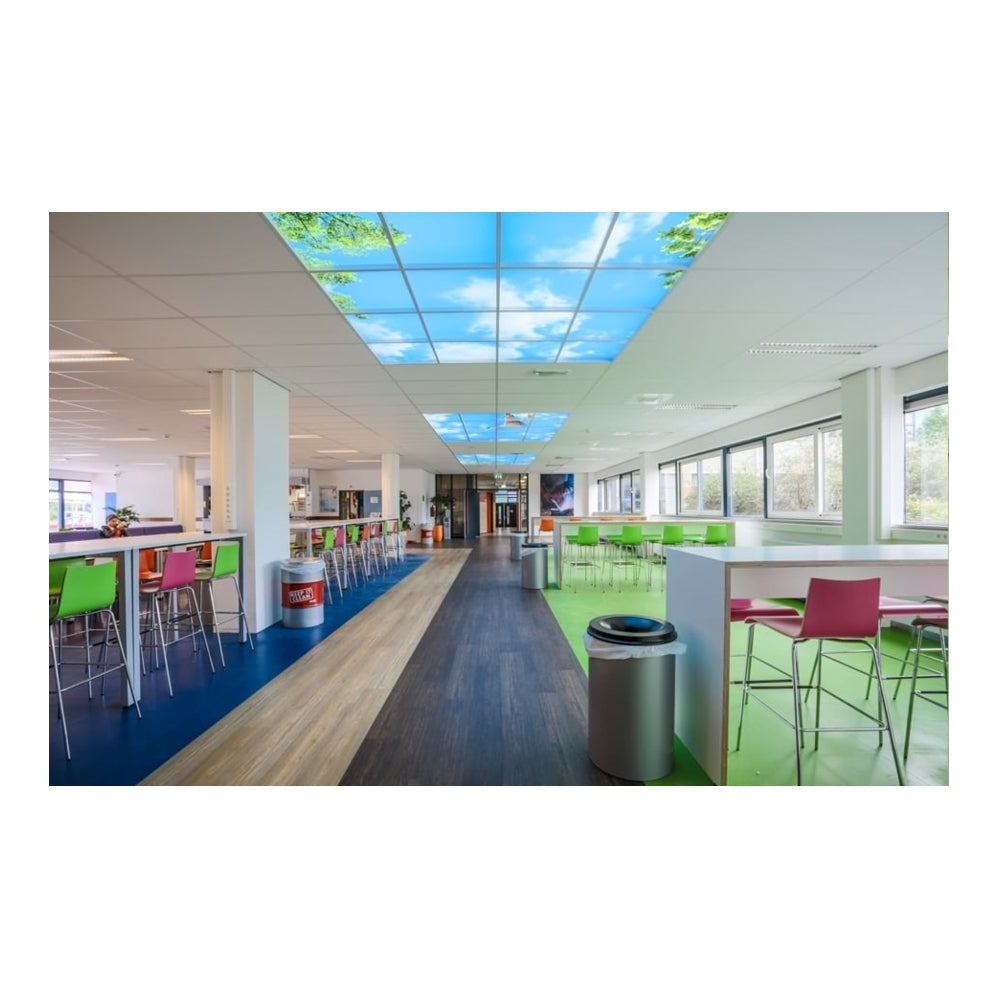 Moderne bedrijfs-kantine met kleurrijke stoelen en tafels, gezien vanuit een diagonaal vooraanzicht, met opvallend verlichte systeemplafondpanelen die een blauwe lucht met wolken en boomtoppen afbeelden.