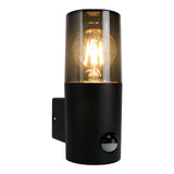 Zwarte moderne buitenwandlamp met sensor en helder glas, vooraanzicht met zichtbare filamentlamp en geïntegreerde bewegingssensor.