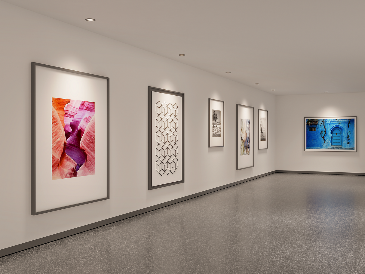 Moderne galerijruimte met witte muren, voorzien van een reeks ingelijste kunstwerken en foto's, weergegeven in een hoekaanzicht met zicht op de linker- en achterwand, onder ingebouwde plafondspotverlichting.
