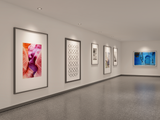 Moderne galerijruimte met witte muren, voorzien van een reeks ingelijste kunstwerken en foto's, weergegeven in een hoekaanzicht met zicht op de linker- en achterwand, onder ingebouwde plafondspotverlichting.