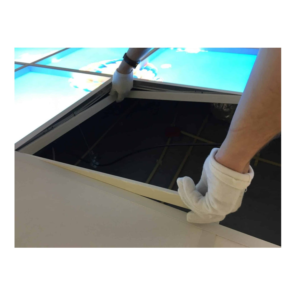 Close-up van een persoon met witte handschoenen die een verlicht systeemplafondpaneel opent vanaf de onderzijde, met zicht op de achterliggende bedrading en constructie.